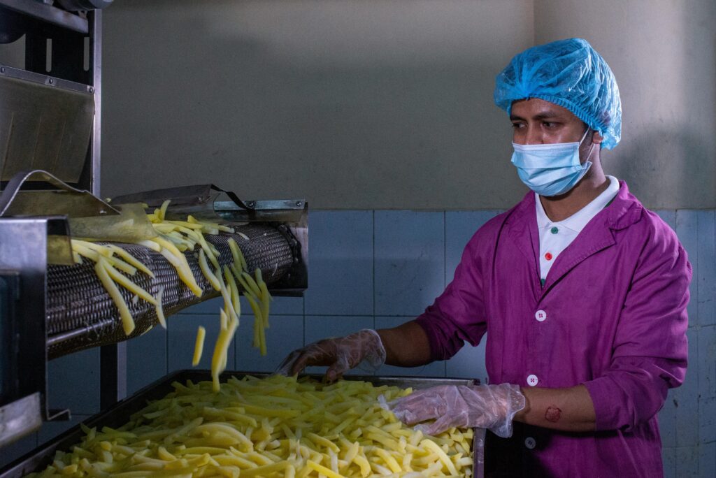 pexels-photo-24394699-24394699 A factory worker in protective gear monitors the production of French fries, ensuring quality control.