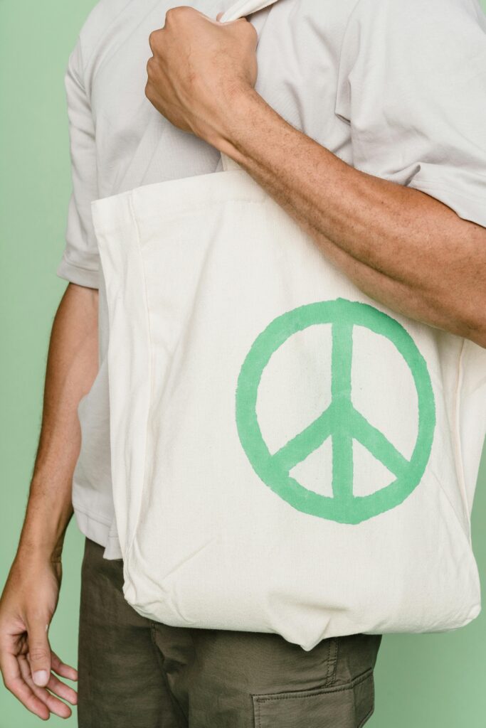 pexels-photo-9324371-9324371 Close-up of a person carrying a tote bag with a green peace symbol, emphasizing sustainability.